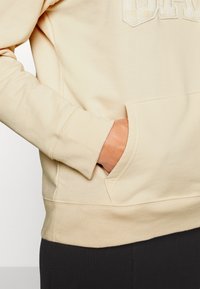 Beige sweatshirt met een kangoeroezak, geribbelde manchetten en zoom. Gedetailleerd met een getextureerd logo op de borst. Zachte stof van een katoenmix.