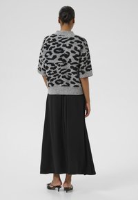 Grey knitted pullover with black leopard print, short sleeves, and ribbed hem, paired with a floor-length black skirt and black heeled sandals.