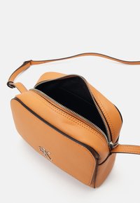 Orange leather crossbody bag with black trim, rectangular shape, zip closure, and a silver logo on the front. Interior is black.