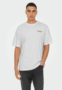 Witte katoenen t-shirt met een ronde hals, korte mouwen en groene en rode tekst "London Fields Specialist" op de linkerborst.