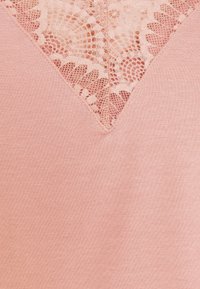 Ljusrosa topp med V-ringning och spetsdetaljer vid halslinjen. Mjuk textur med slät tyg och intrikata spetsmönster.