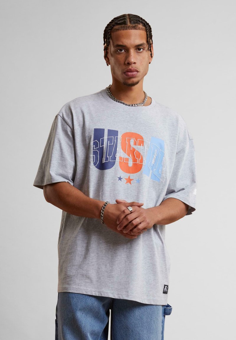 Gray oversized t-shirt made of cotton, featuring a multi-colored "USA" graphic with stars. Short sleeves, crew neck, relaxed fit.