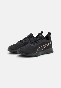 Zapatillas deportivas negras con parte superior de tela texturizada, detalles en dorado y suela de goma flexible. Presenta un cierre con cordones y una pestaña de agarre.