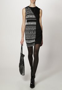 Robe sans manches noir et blanc avec un tissu à motifs d'un côté, noir uni de l'autre ; stylée avec des collants noirs et des bottines brillantes.