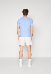 Hellblaues, kurzärmliges Sportshirt mit nahtlosem Design, kombiniert mit beigen Shorts. Das Modell ist von hinten zu sehen.