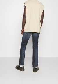 Top sin mangas color beige con un corte relajado, combinado con jeans de mezclilla azul oscuro y zapatos negros. Diseño simple y funcional sin patrones visibles.