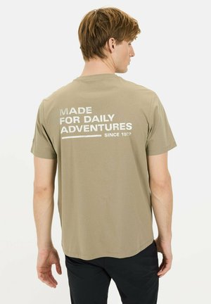 Kortærmet olivengrøn t-shirt med hvid tekst på ryggen, der står "MADE FOR DAILY ADVENTURES" og "SINCE 1917." Standard pasform, bomuldsstof.