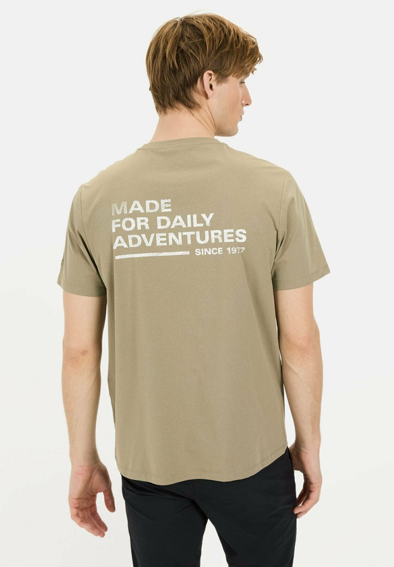 Kortærmet olivengrøn t-shirt med hvid tekst på ryggen, der står "MADE FOR DAILY ADVENTURES" og "SINCE 1917." Standard pasform, bomuldsstof.