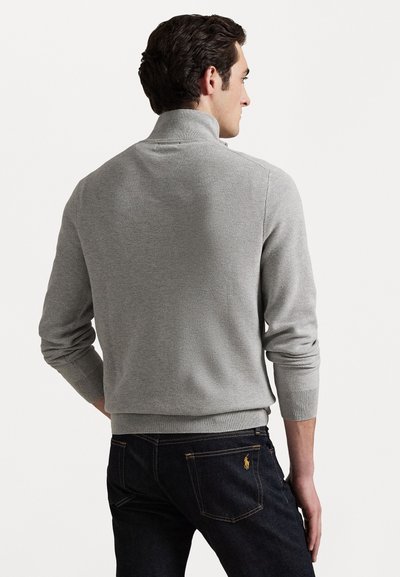 Pullover cinza em malha com gola alta, punhos e barra canelados. Apresenta um padrão texturizado. Usado com jeans escuros.