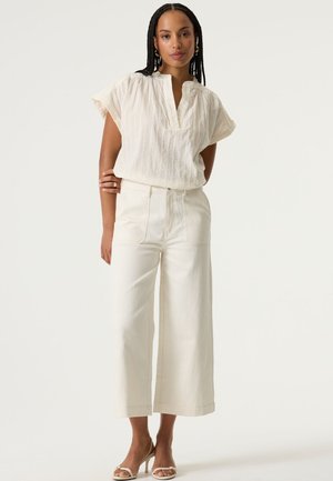 Blouse blanche texturée à manches courtes et col, associée à un pantalon blanc taille haute à jambes larges. Sandales à brides complètent la tenue.