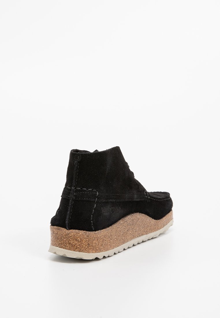 Chaussure cheville en suede noir avec une semelle intermédiaire en liège texturé et une semelle extérieure en caoutchouc. Présente des coutures minimales et une forme arrondie.