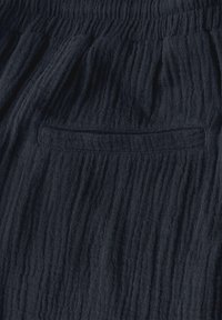 Tmavě modrá texturovaná tkanina s krčeným vzhledem. Obsahuje elastický pás a diskrétní zadní kapsu.