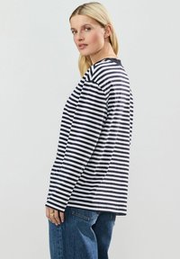 Langærmet stribet skjorte i marineblå og hvid. Har rund hals og afslappet pasform. Parret med blå højtaljede jeans for et afslappet look.