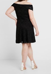 Svart axelbandslös spetsklänning med en åtsittande liv och utsvängd kjol med scallopade kanter. Bärs med vita ankelbandssandaler.