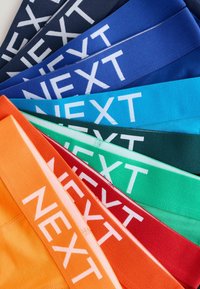 Färgglada tygband med "NEXT"-logotypen, arrangerade i ett staplat mönster. Färgerna inkluderar marinblå, blå, orange, röd, grön och teal.