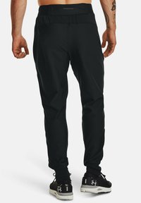 Zwarte sportbroeken met een taps toelopende pasvorm, elastische tailleband en een gladde textuur, gecombineerd met zwarte schoenen met een patroon op de zool.