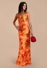 Orangesatin-blumenmuster Kleid mit roten Mustern, figurbetonte Silhouette, Spaghettiträger und fließender Saum. Kombiniert mit einer roten Umhängetasche.