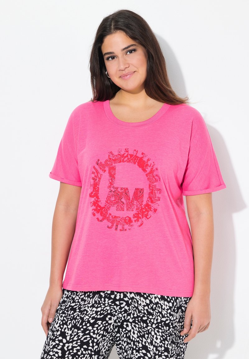 T-shirt in cotone rosa con un design grafico rotondo rosso. Maniche corte e vestibilità rilassata, abbinata a pantaloni a fantasia bianca e nera.