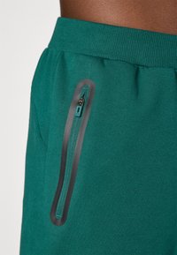 Teal sport shorts med ribbet talje og en sort lynlåslomme på siden. Blød tekstur og afslappet design.