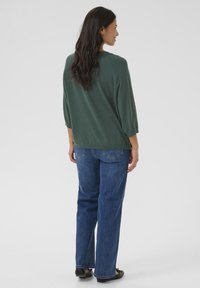 Green, loose-fit sweater with three-quarter sleeves, paired with blue straight-leg jeans. The outfit features a casual and comfortable design.