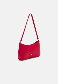 Červená kožená taška přes rameno s tenkým popruhem a malým zlatým logem na přední straně, vystavená na bílém pozadí.