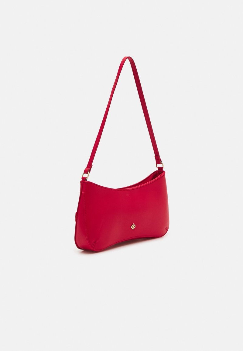 Červená kožená taška přes rameno s tenkým popruhem a malým zlatým logem na přední straně, vystavená na bílém pozadí.