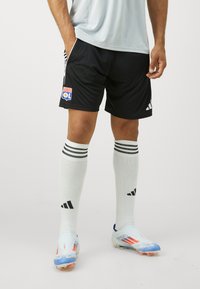Svarte fotballshorts med sidelister, hvite knelange sokker med svarte striper, og flerfargede fotballsko med strømlinjeformet design.