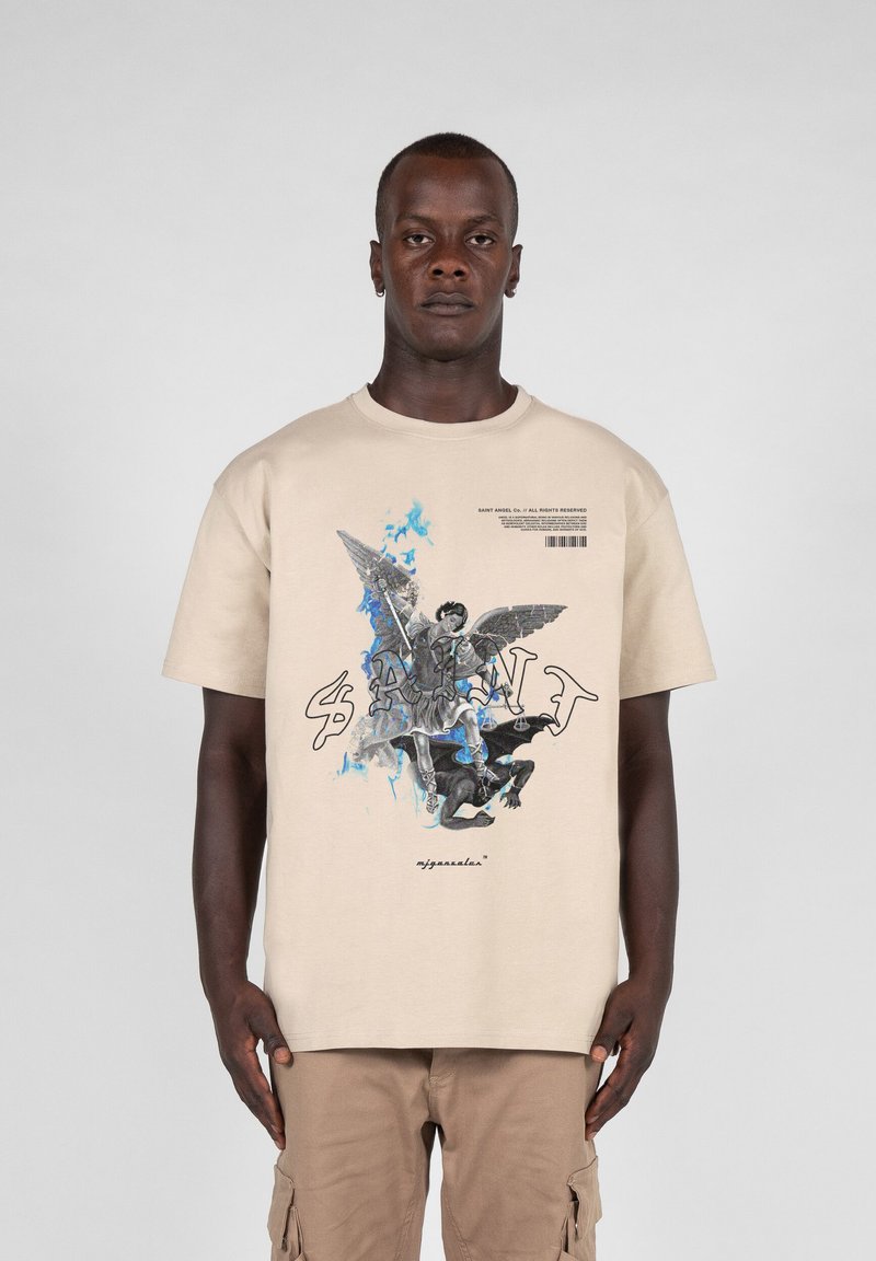 Beżowy bawełniany t-shirt z graficznym nadrukiem anioła oraz postaci w niebieskich i czarnych akcentach. Krótkie rękawy i okrągły dekolt.