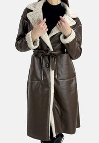 Brauner Mantel aus Kunstleder mit cremefarbenem Kunstpelzkragen und -manschetten. Ausgestattet mit einem Taillengürtel, zwei Fronttaschen und einer Knopfverschluss.