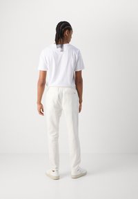 Hvid t-shirt med korte ærmer, parret med lyse, løstsiddende bukser og hvide sneakers, set fra ryggen. Enkelt design, ingen mønstre.