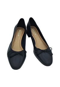 Chaussures plates noires avec un extérieur en cuir souple, bout rond, talon bloc bas et un détail en nœud à l'avant. L'intérieur possède une semelle intérieure beige.