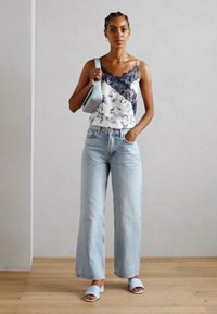 Top sin mangas con un borde de encaje azul marino, tejido blanco con patrones suaves, combinado con jeans de pierna ancha de cintura alta en un azul claro y sandalias también en azul claro.