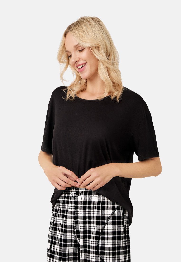 Czarna, krótko rękawowa koszulka o luźnym kroju i okrągłym dekolcie, zestawiona z czarno-białymi spodniami w kratkę z wzorem w szkocką kratę.