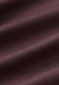 Plis de tissu lisses en violet foncé avec une fine texture côtelée diagonale créant de douces ombres sur la surface.