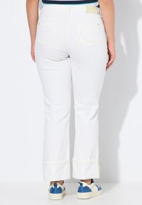 Jeans blancos de campana con dobladillos enrollados y bolsillos traseros con detalles de costura, combinados con zapatillas azules y blancas.