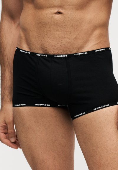 Κοντινό ενός άνδρα που φοράει μαύρα boxer Dsquared2 με ελαστική ζώνη μέσης και λάστιχα στα πόδια με λογότυπο, δείχνοντας το κάτω μέρος του κορμού και το πάνω μέρος των μηρών του.