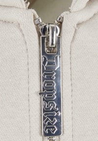 Beige Zip-up Hoodie mit einem silbernen Reißverschluss, der "Dropsize" in einer fetten, stilisierten Schrift zeigt, und einer strukturierten Oberfläche.