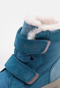 Blå ruskind vinterstøvle med en pelsagtig pink foring og velcro-lukning. Har en blød tekstur og en let glansfuld overflade.