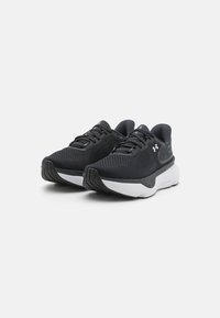 Des chaussures de sport noires en maille respirante avec une finition texturée, dotées d'une semelle blanche et d'une semelle extérieure en caoutchouc noir. Design à lacets.