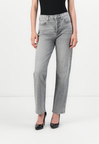 Lichtgrijze high-waisted jeans met een iets relaxte pasvorm. Gemaakt van denim, met voorzakken en een subtiele textuur. Gecombineerd met zwarte hakken.
