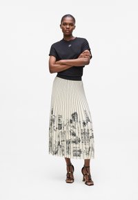 Haut noir à manches courtes et jupe plissée crème avec des dessins de paysage urbain noirs. Sandales à talons noires à lanières. Design simple avec des textures contrastées.