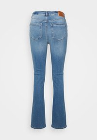 Calças de ganga azul de boca de sino com uma cintura de altura média, dois bolsos traseiros e um rótulo de pele castanha na cintura. Textura suave.