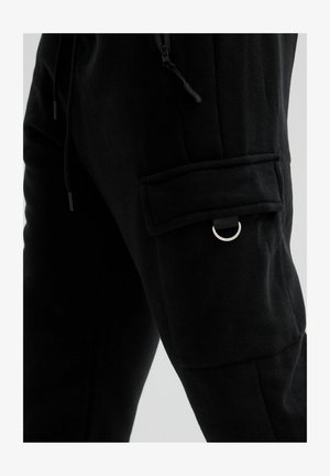 Pantalones negros con un bolsillo con solapa en el muslo que presenta un detalle de anilla en D metálica y un cordón ajustable en la cintura.
