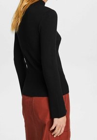 Schwarzer gerippter Pullover mit hohem Kragen, langen Ärmeln und körperbetonter Silhouette, kombiniert mit einem rostfarbenen Rock mit Taschen.