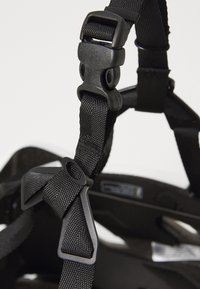 Black helmet strap featuring nylon material, adjustable clips, and loop accents. Textured webbing with a secure buckle for fit adjustment.