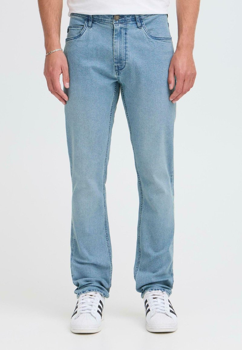Lys blå denimjeans med fem lommer, rett benkutt og subtil fading. Kombinert med hvite sneakers med svarte striper.