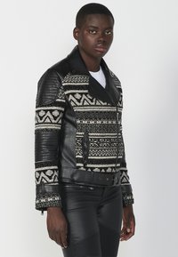 Giubbotto di pelle nera con corpo in maglia a motivo; chiusura con zip diagonale, ampi rever e dettagli in pelle a costine su spalle e maniche.
