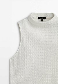 Haut blanc sans manches texturé avec col montant et une étiquette de marque noire à l'encolure.