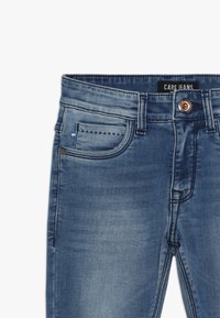 Džínové kalhoty ve středně modré barvě s vybledlým povrchem, s klasickým pětipocket designem, měděným knoflíkem a prošívanými detaily.