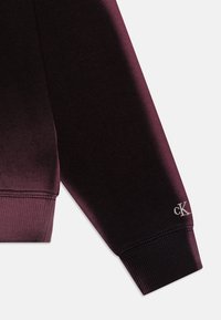 Fioletowy gradientowy rękaw bluzy z prążkowanymi mankietami i srebrnym haftowanym logo "CK". Miękka tkanina o gładkiej fakturze.